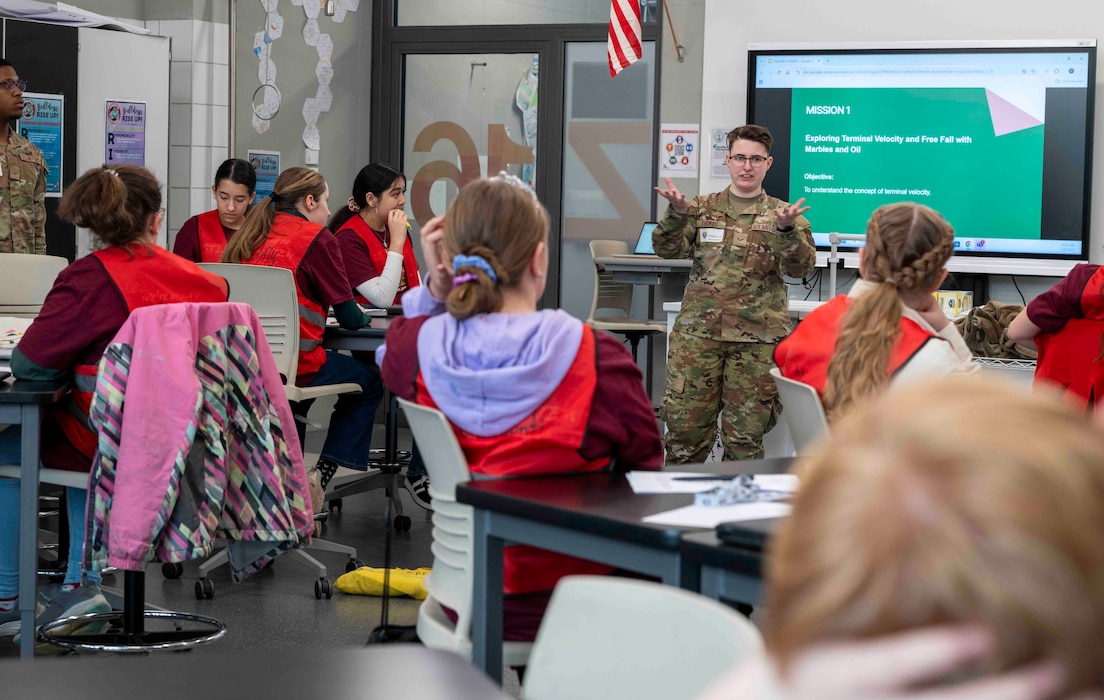 An Airman speaks in front of a classroom of middle school students