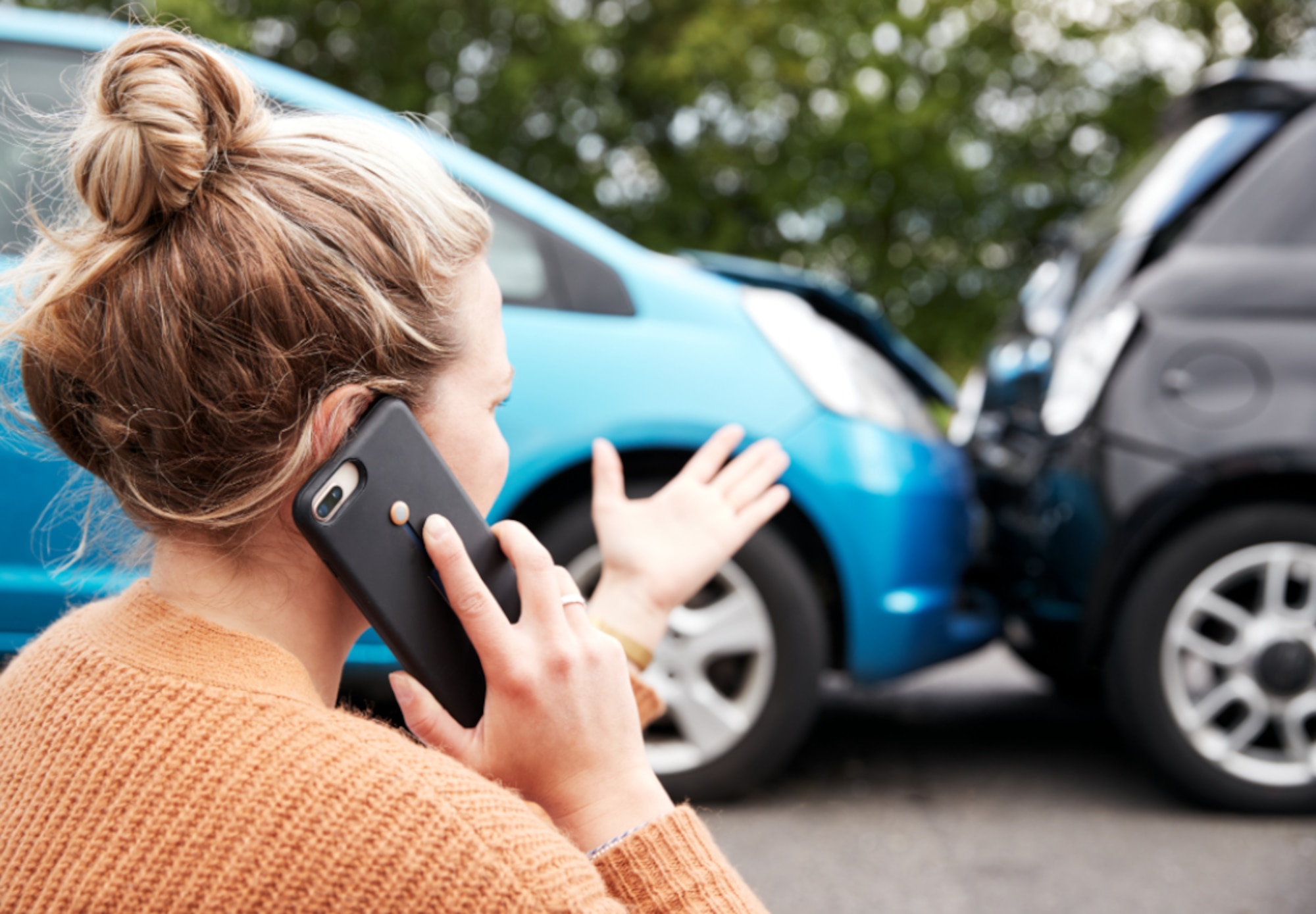 A stock image depicting a women on the phone looking at a car crash.