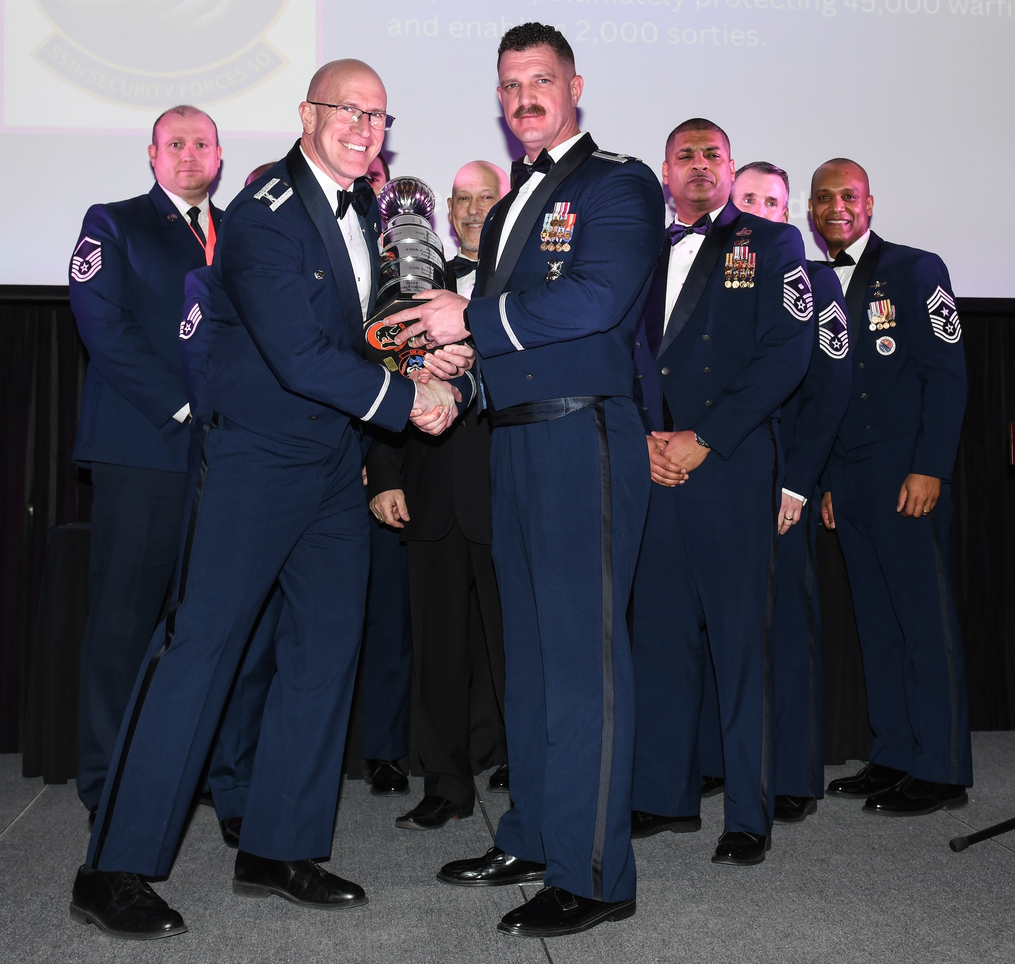 55th Wing Commander Col. Mark Howard hands the Olmstead-McKone trophy to Lt. Col. Andre Ferguson, 55th Security Forces Squadron commander, at the 2024 Annual Awards banquet the Beardmore Event Center in Bellevue, Neb. on Feb. 8, 2025. The trophy recognizes the best unit in the 55th Wing, and emphasizes the unit's mission accomplishments, community support, innovative initiatives, and other arards and recognition. (U.S. Air Force photo by Chad Watkins)