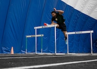 Nasir Dilworth, Minot State University track and field hurdler, jumps over a hurdle in The Bubble at Minot Air Force Base, North Dakota, Feb. 11, 2025. In track and field, hurdling is an event where athletes jump over hurdles while racing to finish a set distance as quickly as possible. (U.S. Air Force photo by Senior Airman Kyle Wilson)