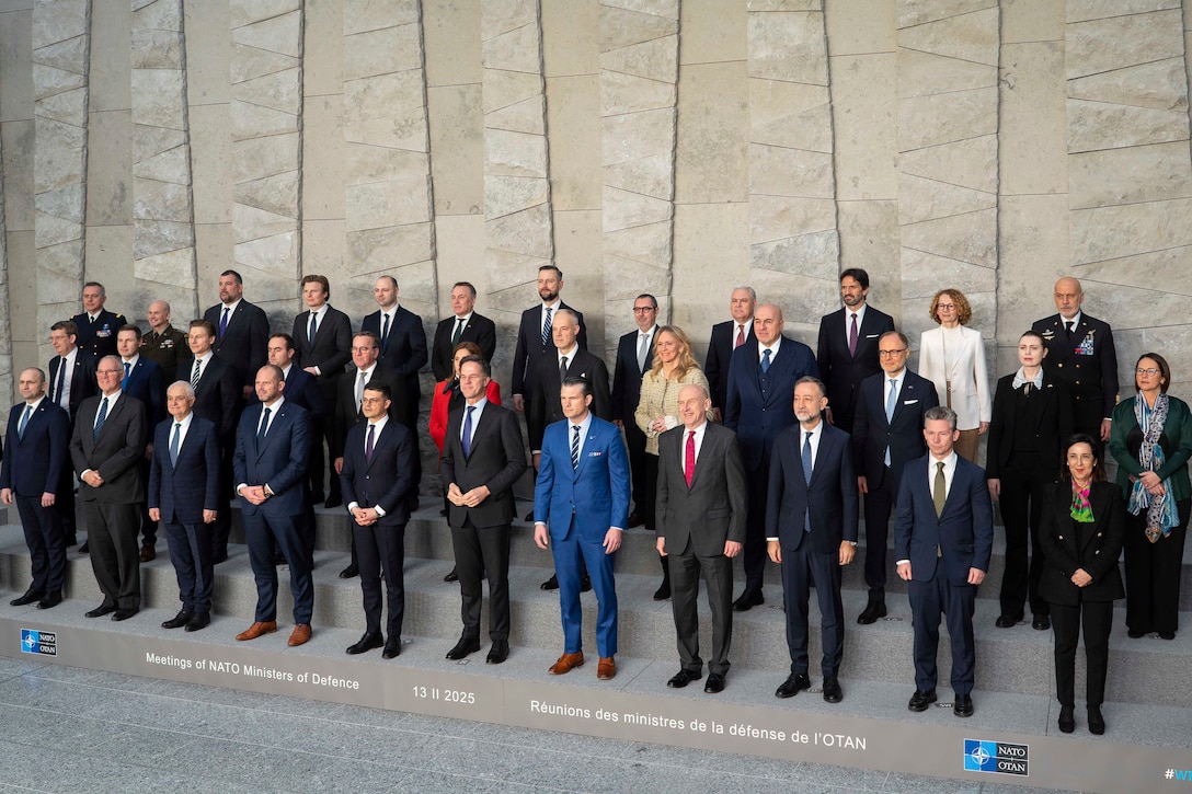 A group of government officials in suits stand and pose on raised platforms for a photo.