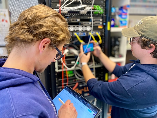 Student writes on iPad while other student takes photo of electronics tower