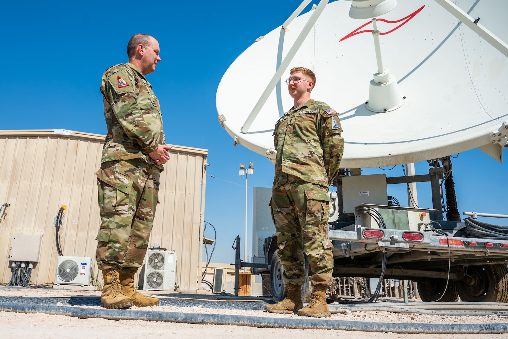 Two military members stand in from of a satellite dish