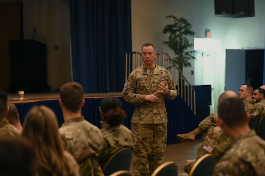  A man in military uniform addresses an audience, gesturing with his hand.