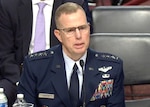 A man in a dress military uniform is sitting at a table talking in a direction off screen to the right.