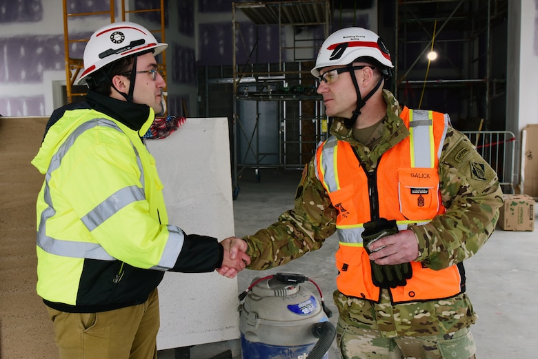U.S. Army Corps of Engineers Command Sgt. Maj. Douglas Galick presents Alec Bissell, civil engineer in the Eastern Tennessee Resident Office, with a coin recognizing excellence during a visit Feb. 12, 2025, to the K-25 Viewing Platform Building construction site in Oak Ridge, Tennessee. The Nashville District is managing construction for the U.S. Department of Energy’s Oak Ridge Office of Environmental Management. The building will provide a historic lookout over the footprint of where the K-25 Building once stood, and the Oak Ridge Diffusion Plant produced uranium during World War II as part of the Manhattan Project. (USACE Photo by Lee Roberts)