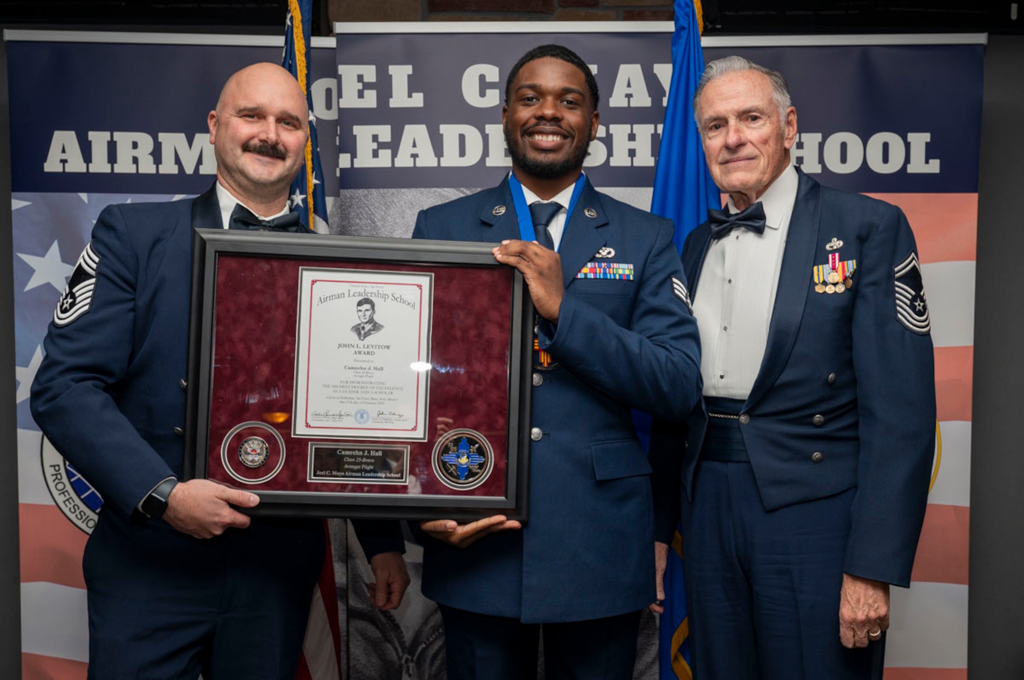 U.S. Air Force Senior Airman Camrehn Hall, center, Airman Leadership Graduate, accepts the John L. Levitow Award from retired Chief Master Sgt. Richard McElderry, right, and U.S. Air Force Chief Master Sgt. Jon Adams, 49th Operations Group senior enlisted leader, during the graduation of Joel C. Mayo ALS Class 25-B at Holloman Air Force Base, New Mexico, Feb. 7, 2025. The John L. Levitow Award is presented to the student demonstrating the highest level of leadership and scholastic performance and is partially determined by the assignment of points by their peers. (U.S. Air Force photo by Senior Airman Michelle Ferrari)