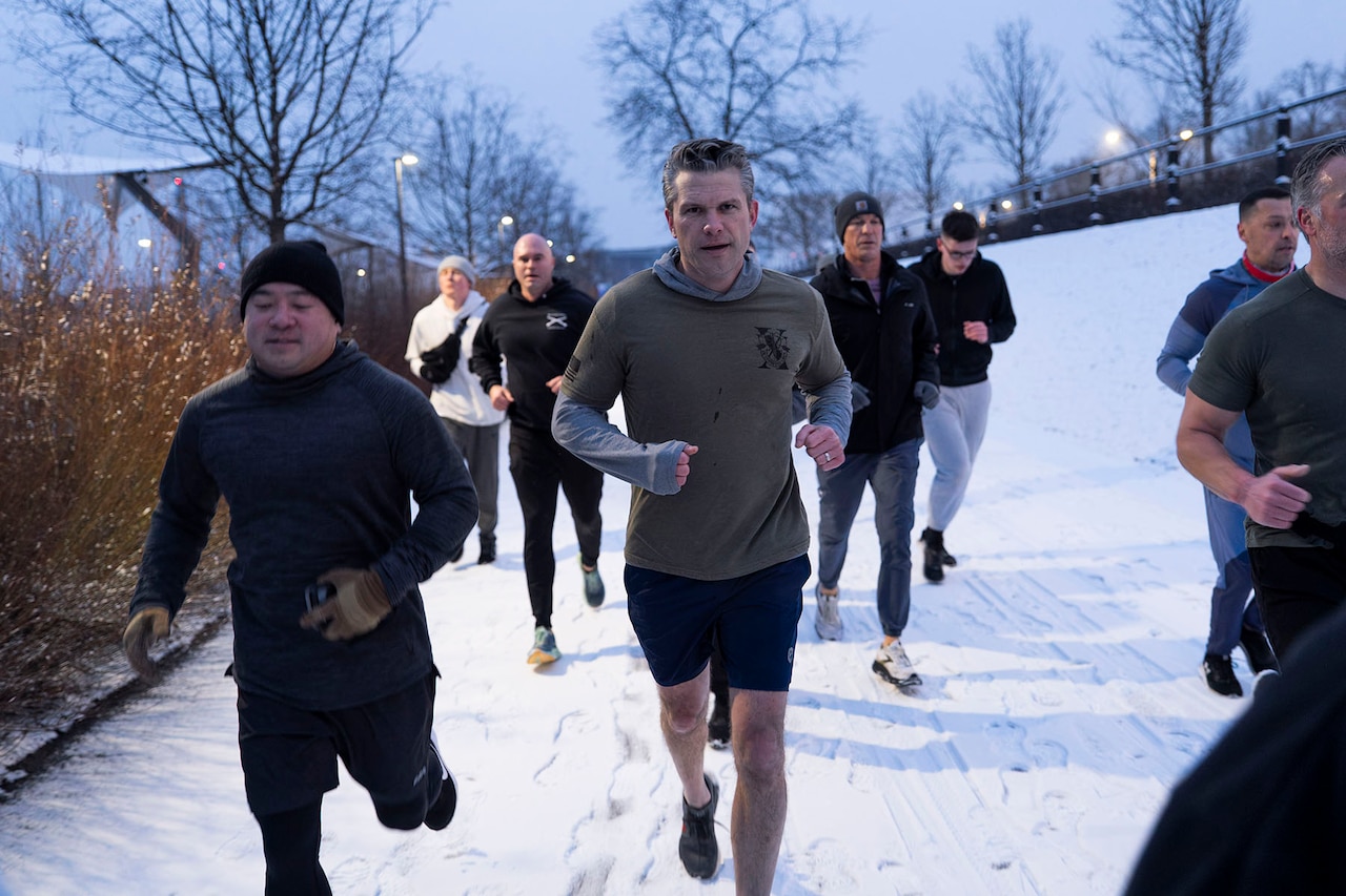 Defense Secretary Pete Hegseth runs surrounded by several service members.