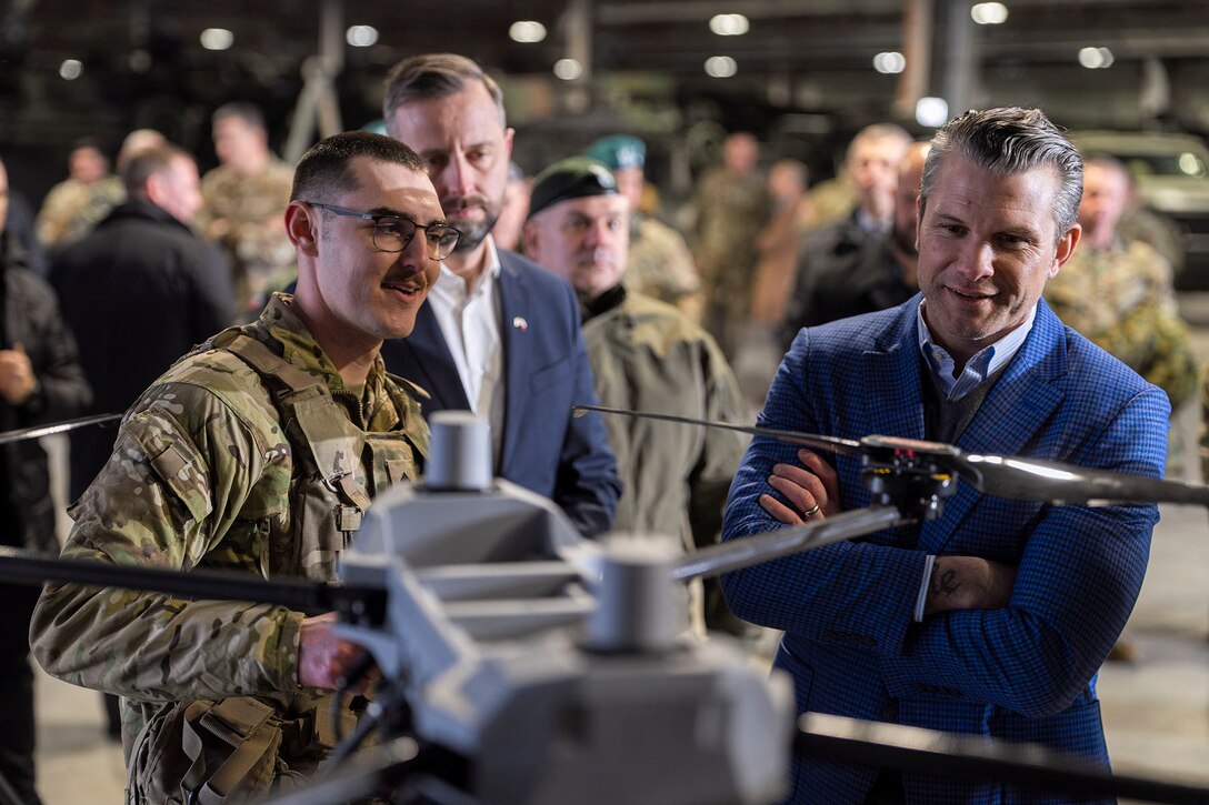 Two government officials look at a drone that a soldier is commandeering.