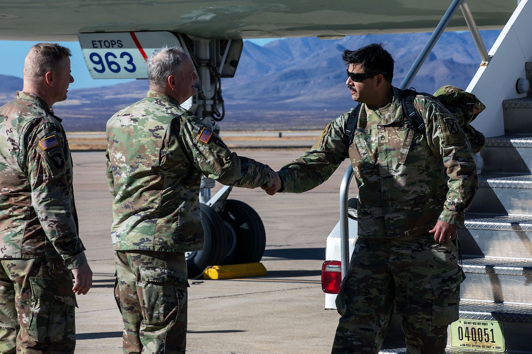 Two soldiers face another soldier exiting the stairs outside an aircraft while one soldier shakes the existing soldier's hand.