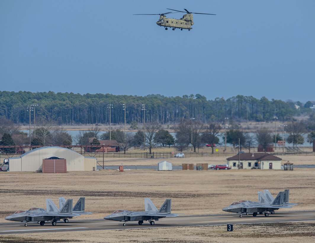 Chinook helicopter flies in the sky above F-22 Raptors