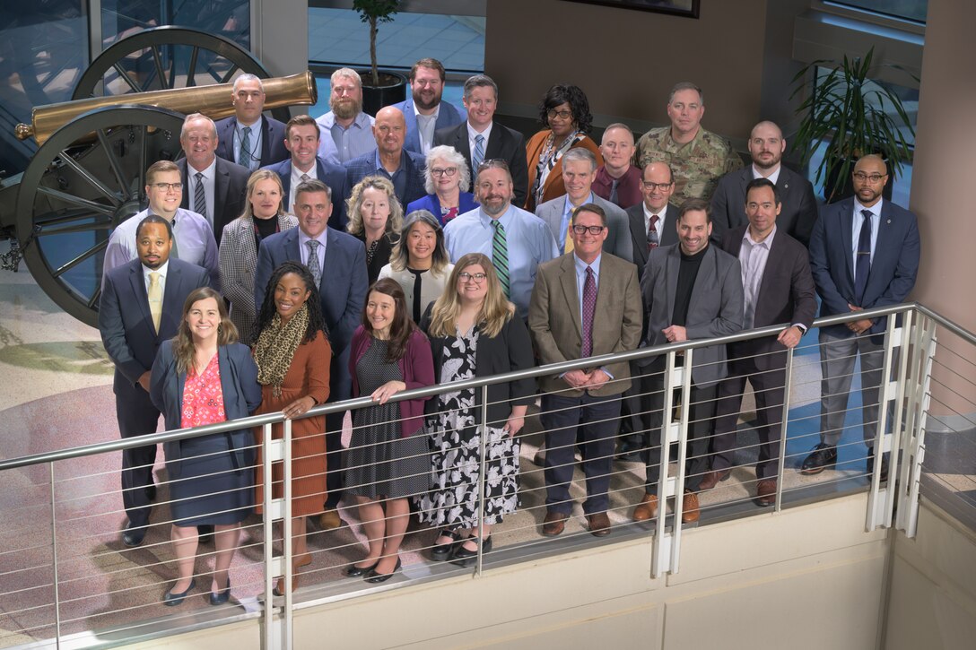 Almost 25 men and women stand near a railing
