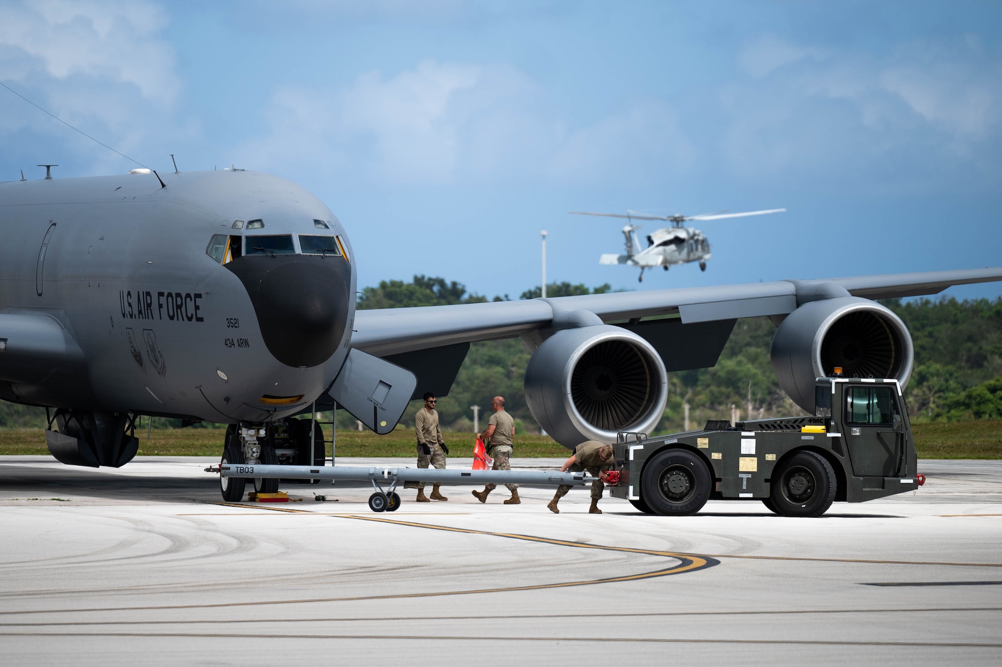 Ground crews work on A KC-135R Stratotanker as a helicopter takes off in the background