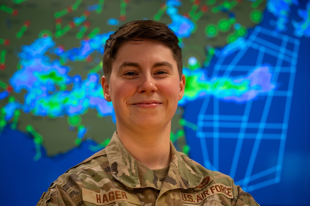 U.S. Air Force Tech Sgt. Victoria Hager is seen from the shoulders and up standing before a screen displaying a synoptic weather chart.