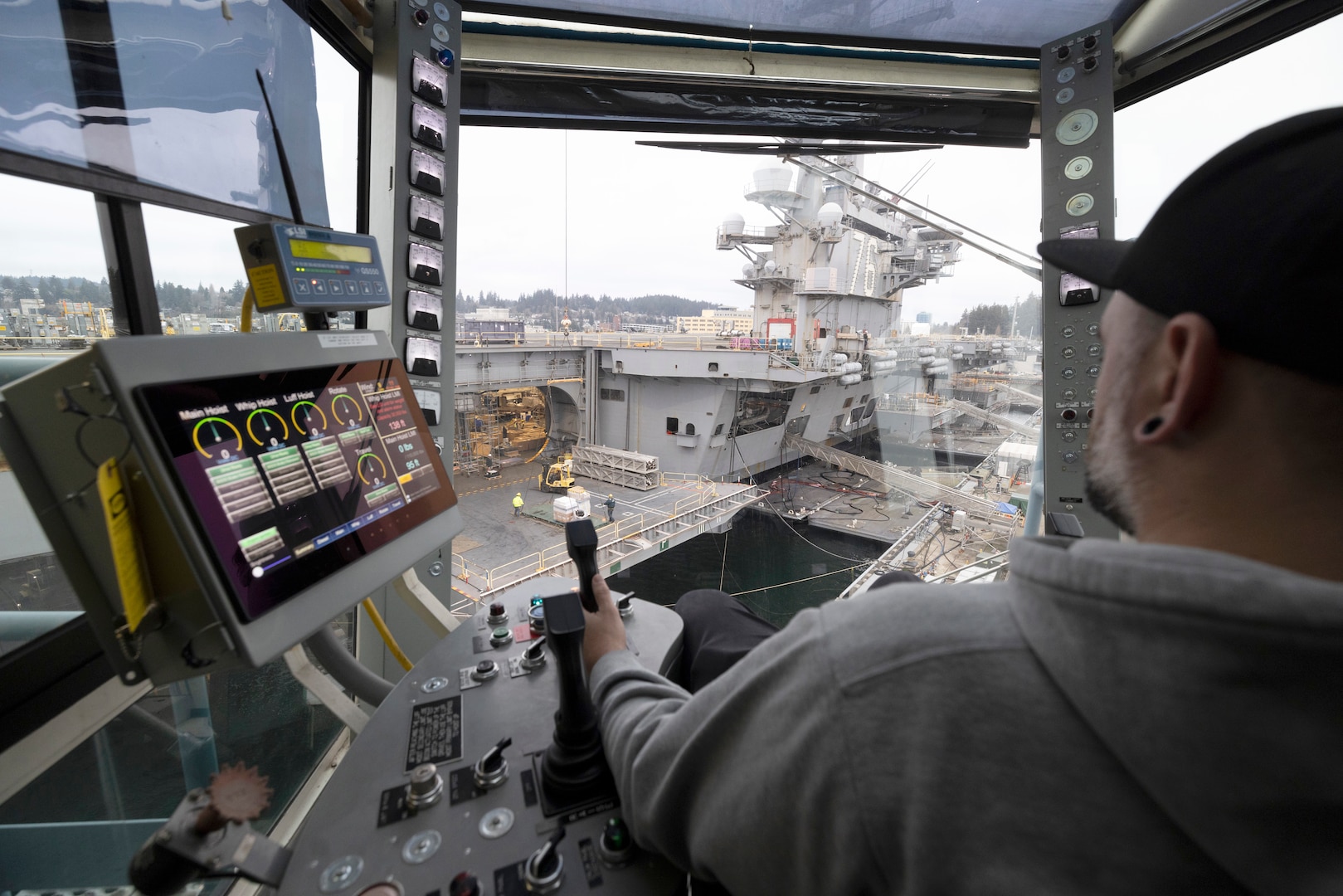 Andrew Babbitt, crane operator, Code 740, Riggers, uses newly upgraded Portal Crane 62 to lower equipment to the hangar bay of USS Ronald Reagan (CVN 76), Jan. 21, 2025, while working along Pier Bravo at Puget Sound Naval Shipyard & Intermediate Maintenance Facility in Bremerton, Washington. (U.S. Navy photo by Wendy Hallmark)