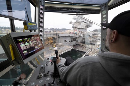 Andrew Babbitt, crane operator, Code 740, Riggers, uses newly upgraded Portal Crane 62 to lower equipment to the hangar bay of USS Ronald Reagan (CVN 76), Jan. 21, 2025, while working along Pier Bravo at Puget Sound Naval Shipyard & Intermediate Maintenance Facility in Bremerton, Washington. (U.S. Navy photo by Wendy Hallmark)