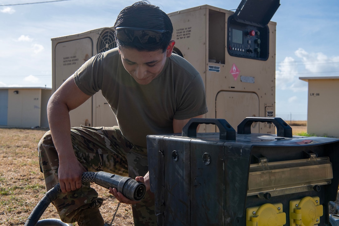 A service member holds a hose attachment to set up an air conditioning system outdoors.