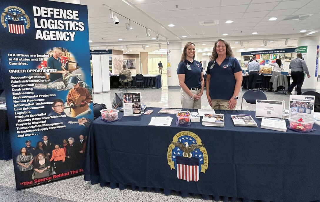 Photo shows two women standing behind table at a recruitment fair