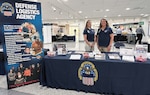 Photo shows two women standing behind table at a recruitment fair
