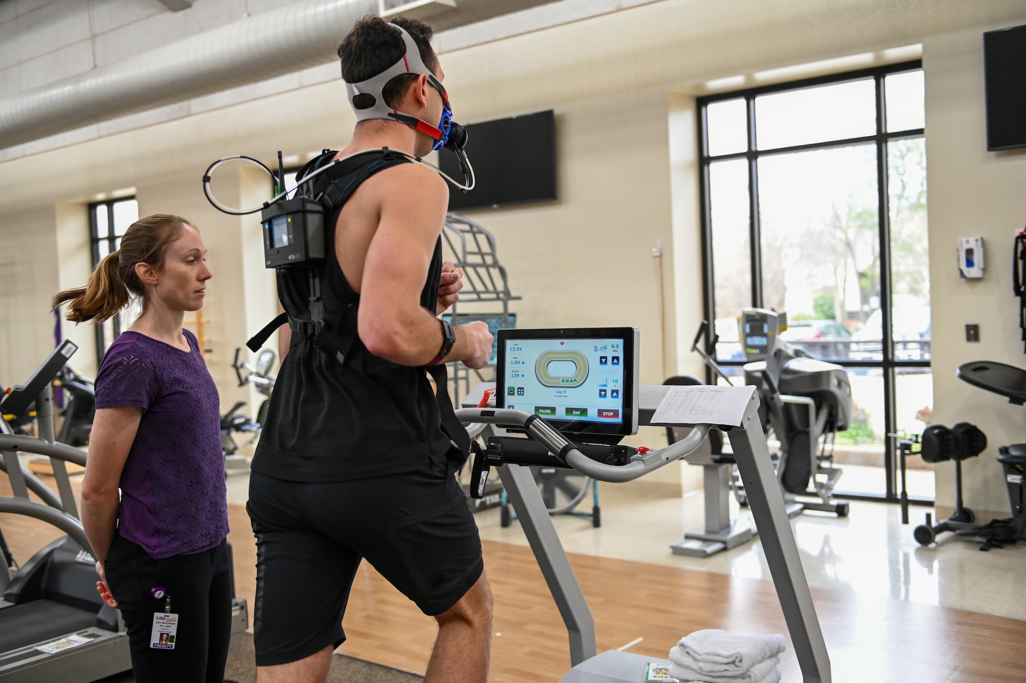 A physical therapist monitors a man while he runs on a treadmill.