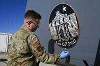 Senior Airman Nathen Willms, a 433rd Maintenance Squadron aircraft structural maintenance technician, applies a new logo to a 433rd Airlift Wing C- 5M Super Galaxy on Feb. 1, 2025, at Joint Base San Antonio-Lackland, Texas.
