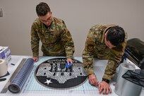 Senior Airman Nathen Willms and Senior Airman Skylar Warren, 433rd Maintenance Squadron aircraft structural maintenance technicians, prep a new logo designed to go on a C-5M Super Galaxy Feb. 1, 2025, at Joint Base San Antonio-Lackland, Texas.