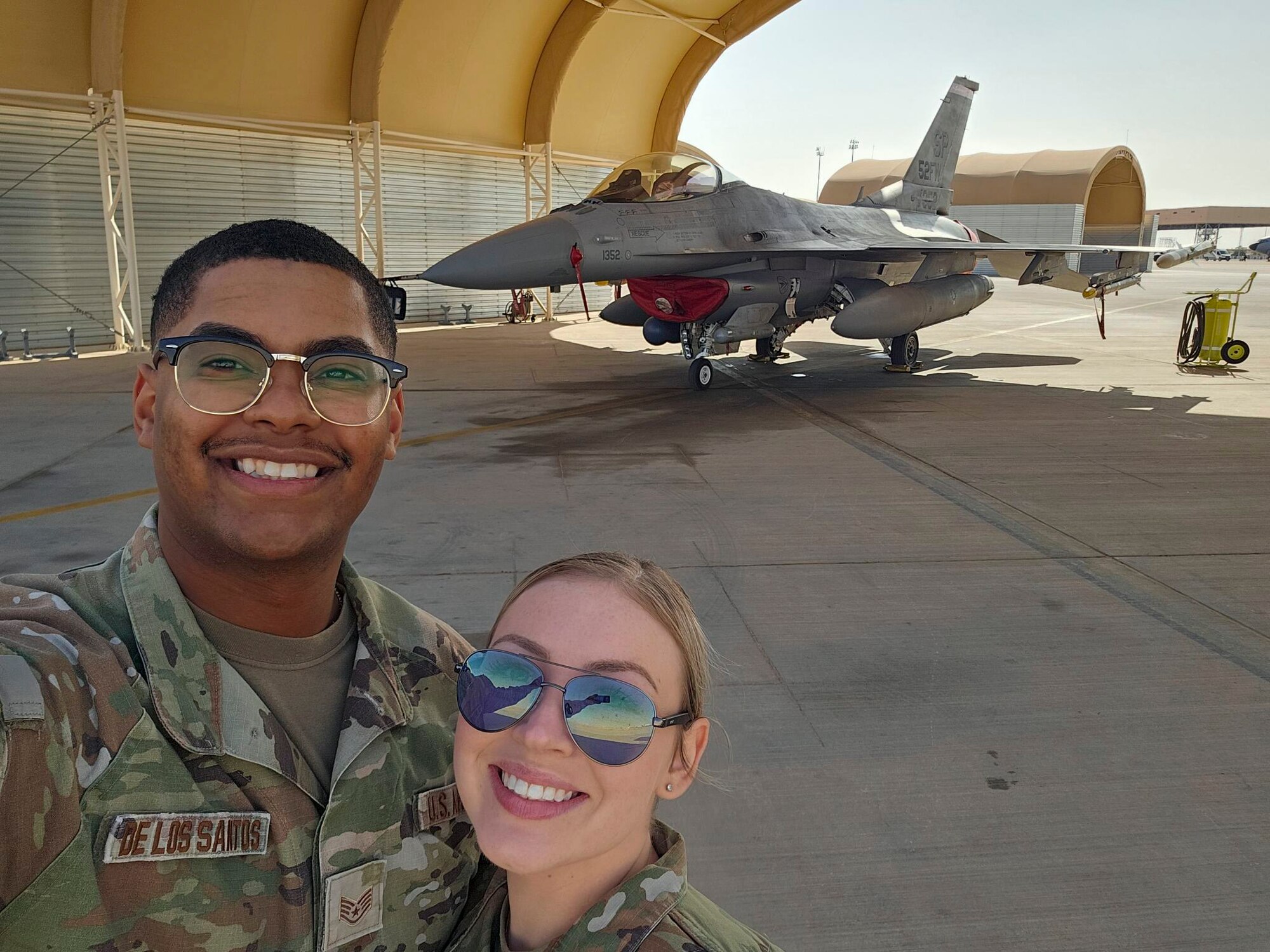 U.S. Air Force Staff Sgt. Hector De Los Santos, 378th Expeditionary Force Support Squadron lodging noncommissioned officer in charge, and U.S. Air Force Senior Airman Hana De Los Santos, 378th Expeditionary Force Support Squadron command support staff, pose in front of an F-16 Fighting Falcon in a U.S. Central Command area of responsibility, Dec. 1, 2024.
