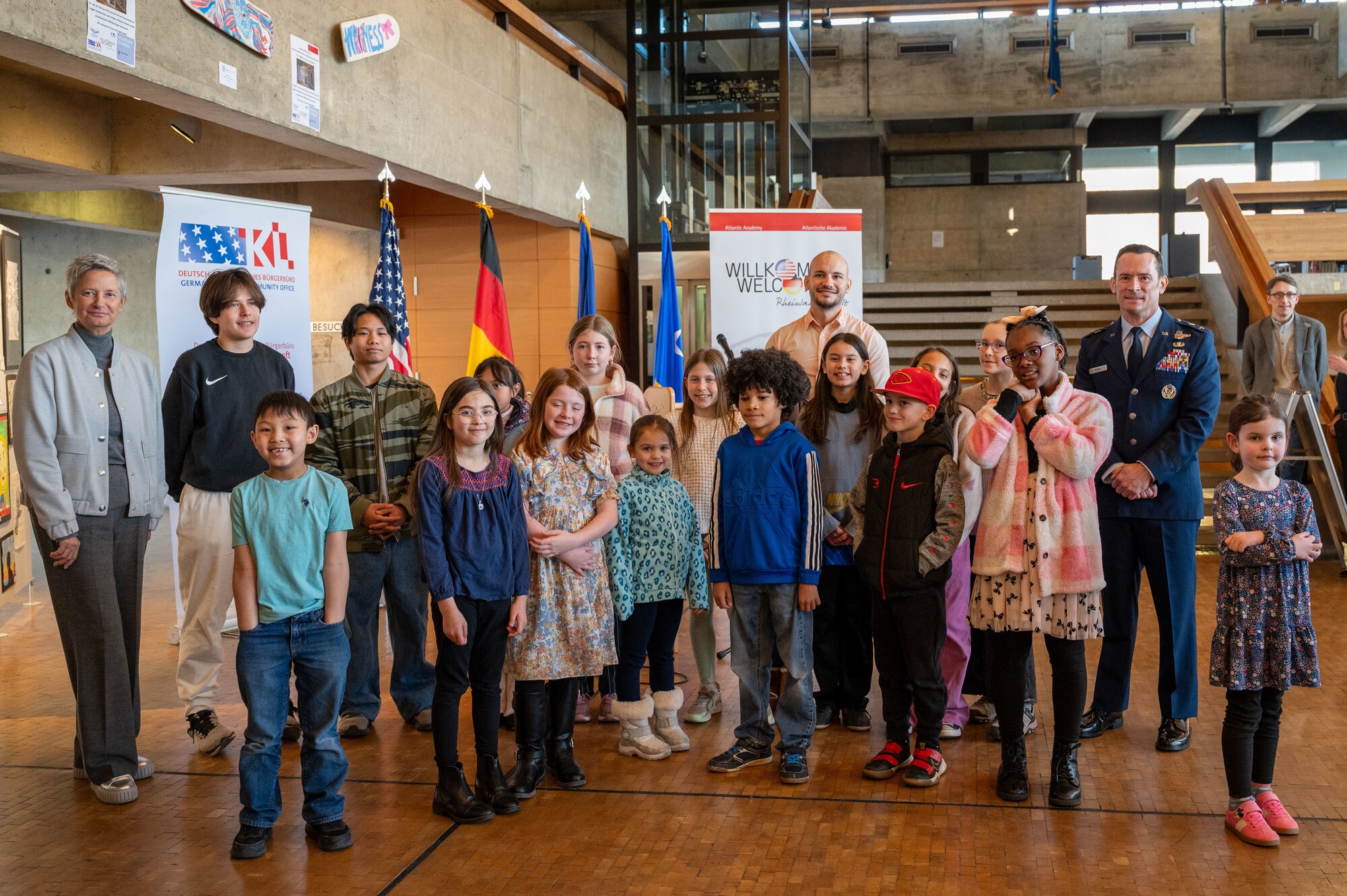 Beate Kimmel, Lord Mayor of Kaiserslautern, Germany, U.S. Air Force Maj. Gen. Paul D. Moga, Third Air Force commander, and children pose for a photo at an art exhibition opening for the 22nd German American Community Office anniversary in Kaiserslautern, Germany, Feb. 18, 2025. The Kottenschule, Burggymnasium, Vogelweh Elementary School, Kaiserslautern and Ramstein Middle School presented 20 artworks for the exhibition, showcasing the ongoing partnership between the military community and host nation.
