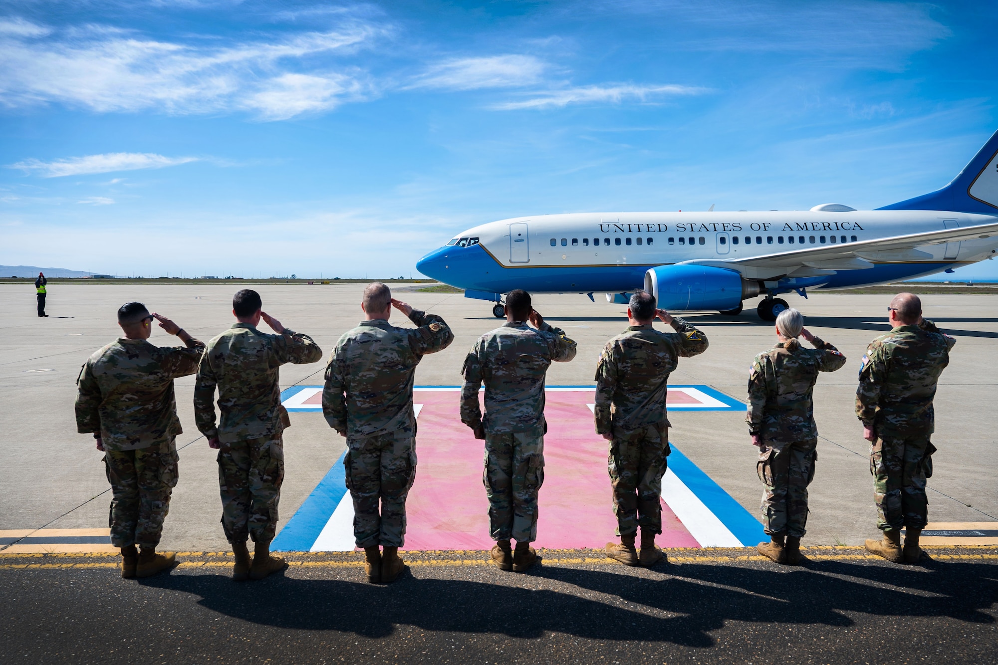 Military members salute a taxiing aircraft on the flight line.