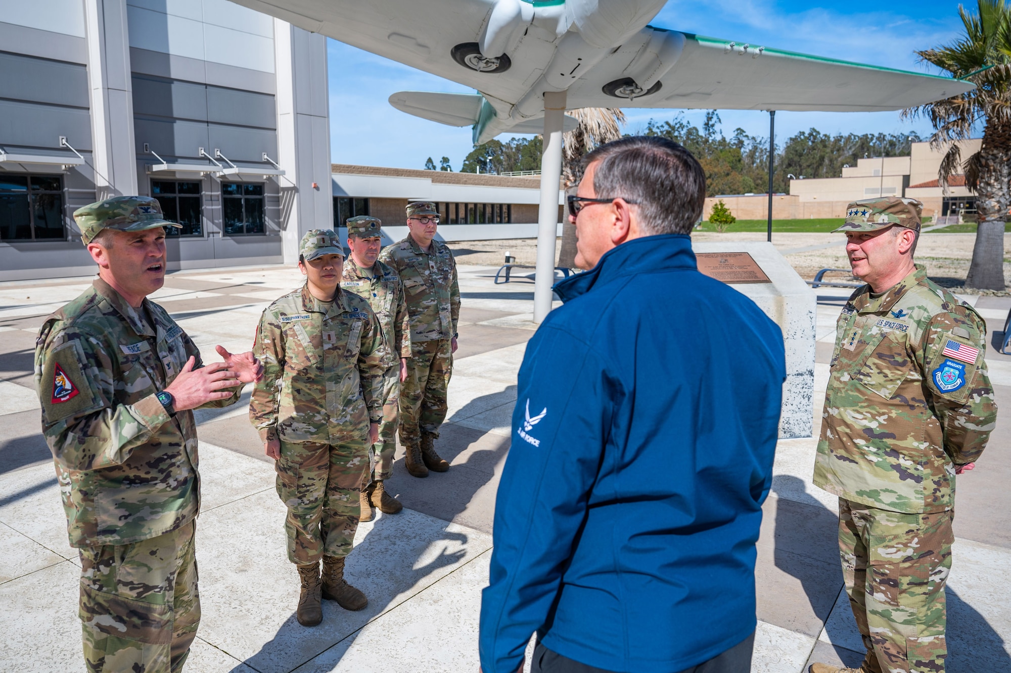 Military members in uniform talk outside in a courtyard.