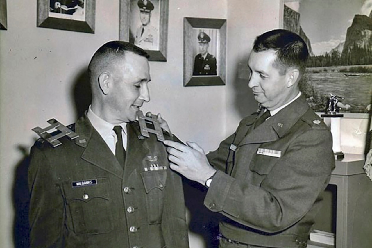 A man places captain bars on another man’s shoulder.