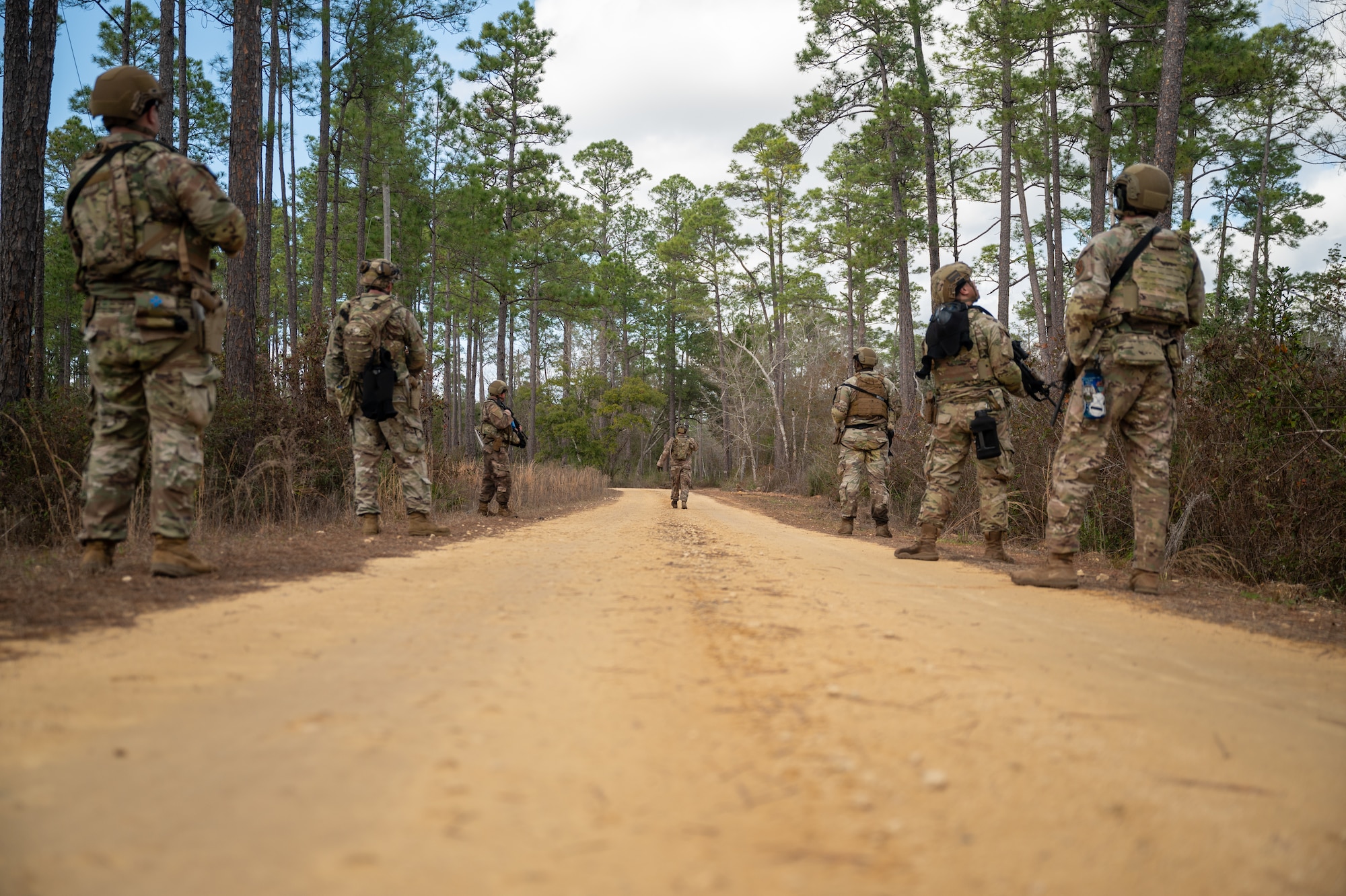 Airmen are seen on a dirt road walking in formation along the edges of the road. They are looking around for any threats as they walk to their next point.