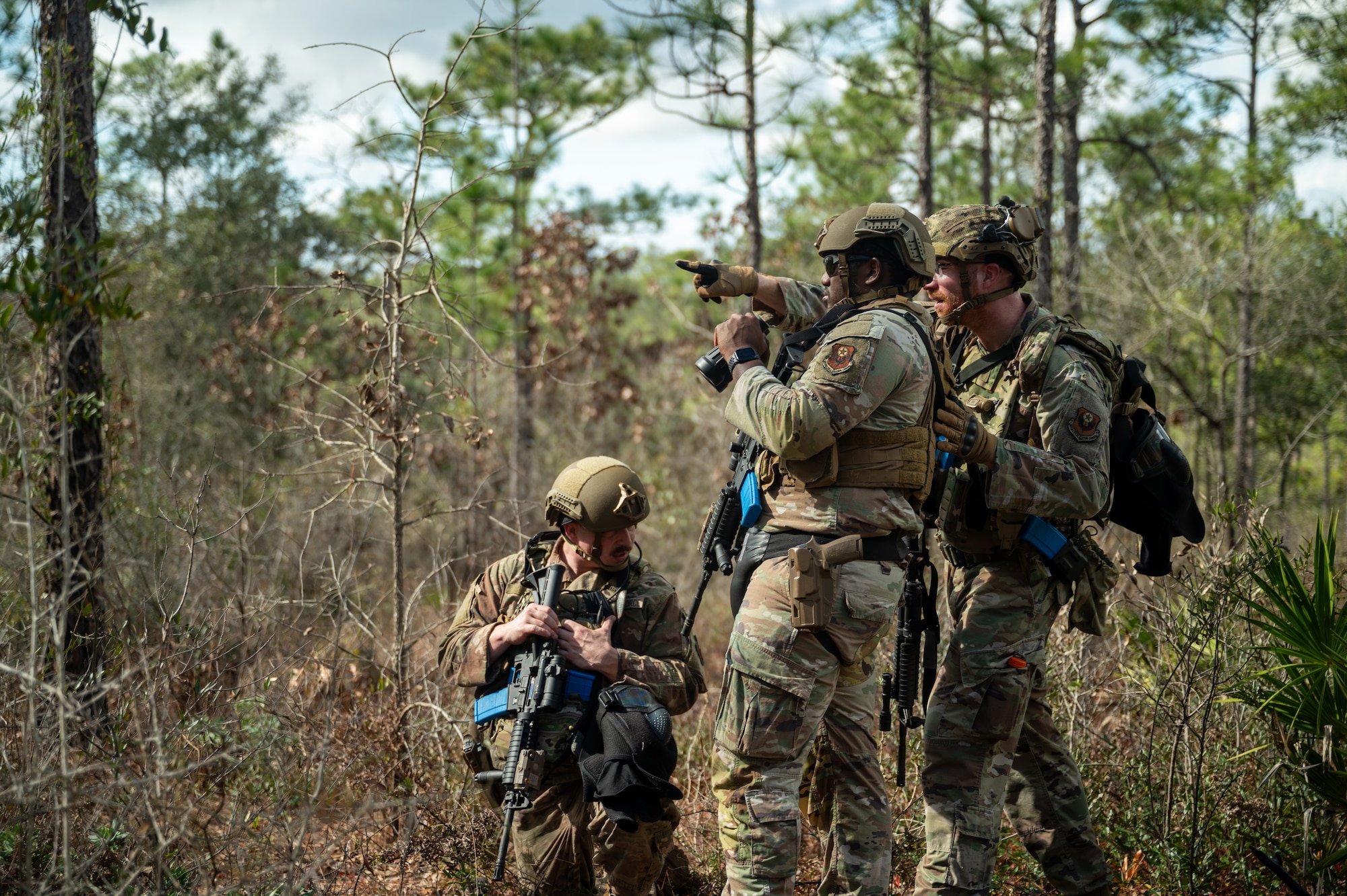 Airmen during a field training exercise in the woods. An Airman is pointing out a spot for another Airman to get a closer look with binoculars.
