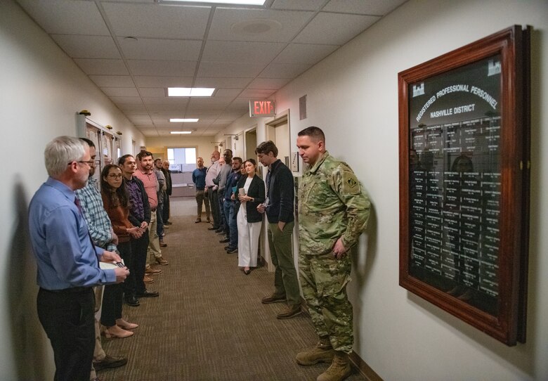 a group of professionally dressed people stand in a hallway while a man speaks to them