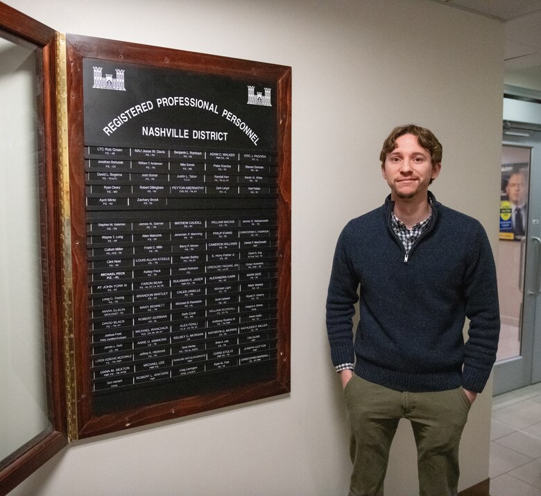 a man stands beside a board of nameplates