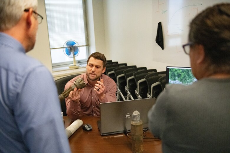 a man holds up a drill bit while talking to two other men