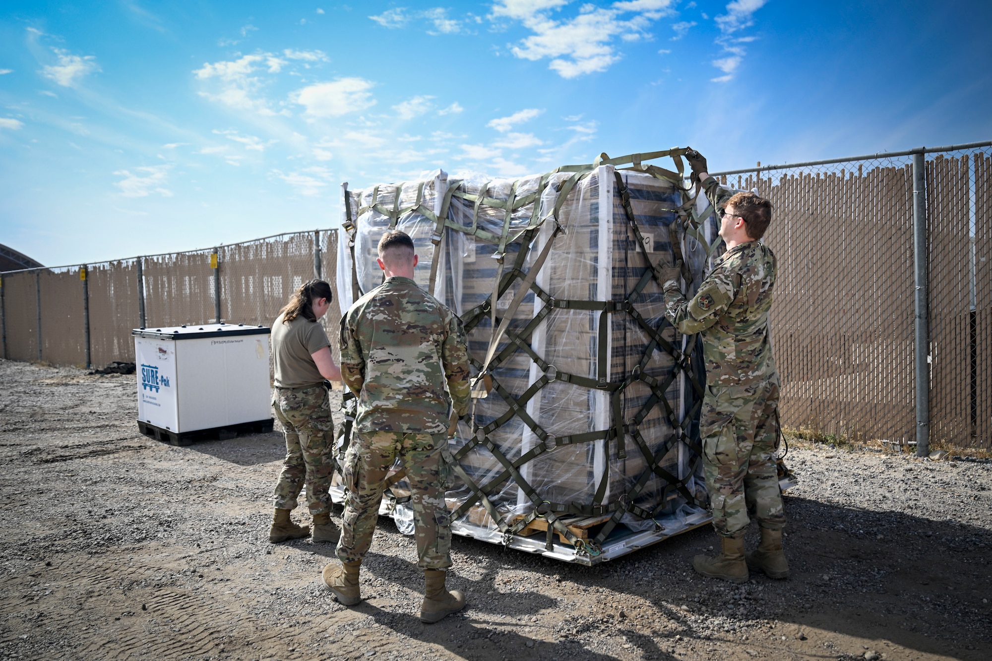 Three U.S. Air Force Airmen unpack a pallet of boxes.