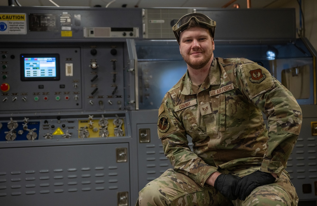 Air Force maintainer poses in front of a hydraulics test apparatus