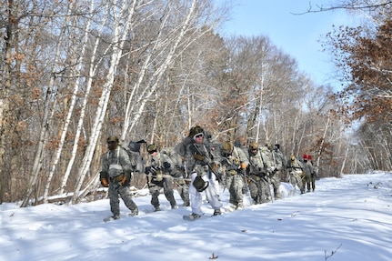 Airmen conduct a long-distance ruck during the Air National Guard’s Cold Weather Operations Course at Camp Ripley Training Center, Minn., followed by two aerospace medical specialists wearing red hats, assigned to the 148th Fighter Wing, Minnesota Air National Guard, Feb. 6, 2025.  Three aerospace medical specialists provided medical education and response to 70 students from 37 Air National Guard Wings attending the course designed to prepare service members for deployments to cold weather regions.