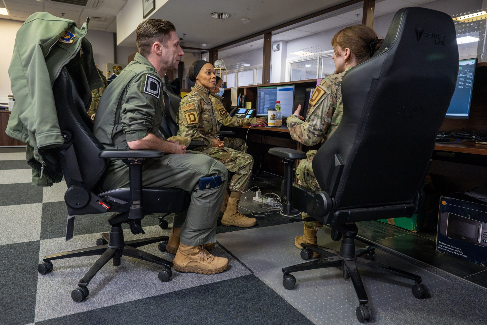 U.S. Air Force Senior Airman Elizabeth Long, right, 100th Operations Support Squadron airfield management shift lead, teaches Col. Ryan Garlow, left, 100th Air Refueling Wing commander, and Chief Master Sgt. Tiffany Griego, 100th ARW command chief, the importance of maintaining airfield operations paperwork during a “Day in the Life” integration with the 100th OSS at RAF Mildenhall, England, Feb. 21, 2025.