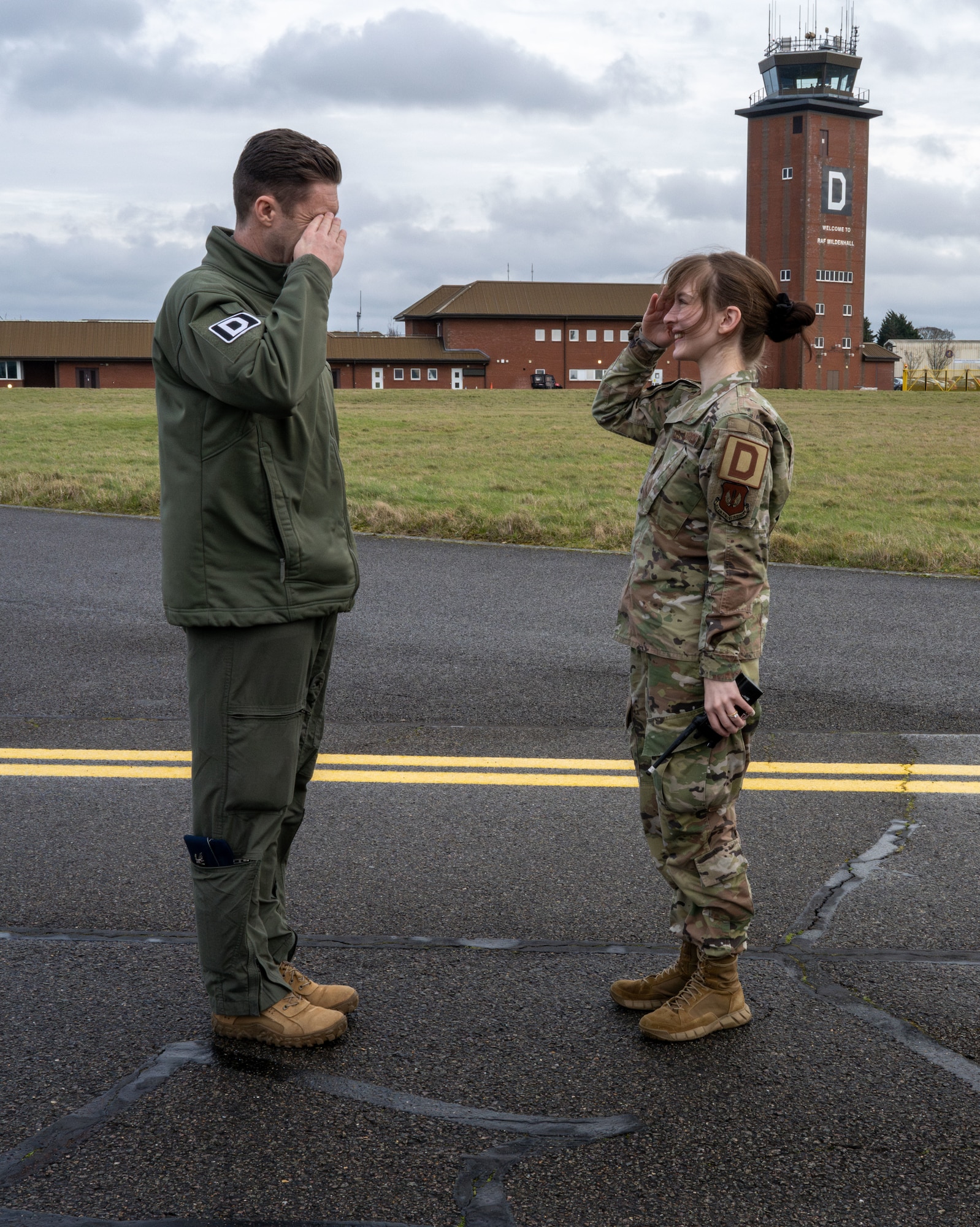 U.S. Air Force Senior Airman Elizabeth Long, right, 100th Operations Support Squadron airfield management shift lead, renders a salute to Col. Ryan Garlow, 100th Air Refueling Wing commander, after being coined for a “Day in the Life” integration with the 100th OSS at RAF Mildenhall, England, Feb. 21, 2025.