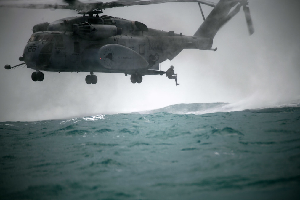 A diver jumps out of a helicopter into rough waters on a cloudy, gloomy day.