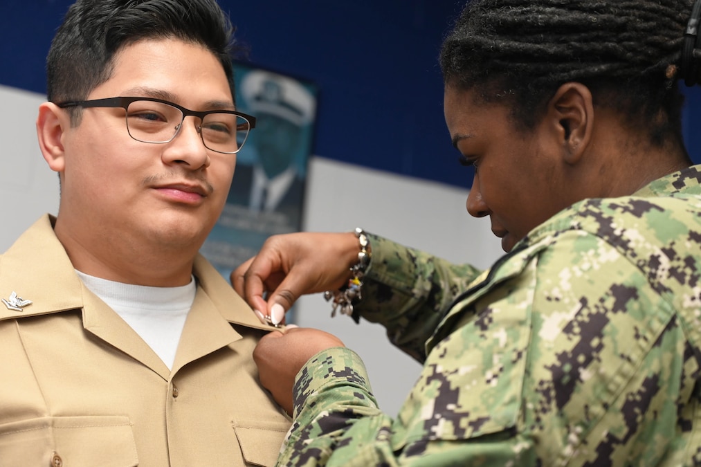 A close-up of a sailor getting a pin on their collar by a fellow sailor.