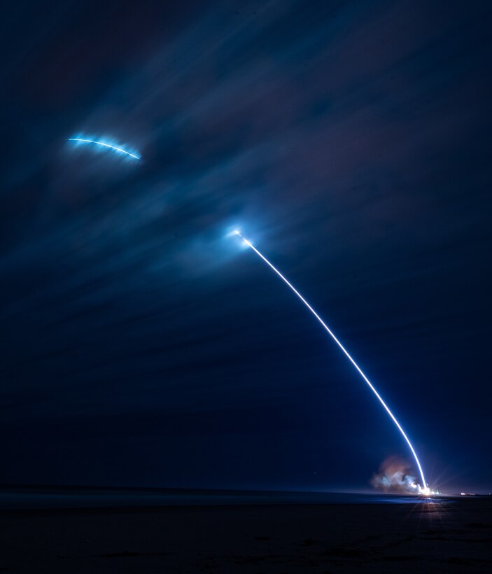 A streak of blue light lifts from the ground and heads upwards. into a nighttime sky.
