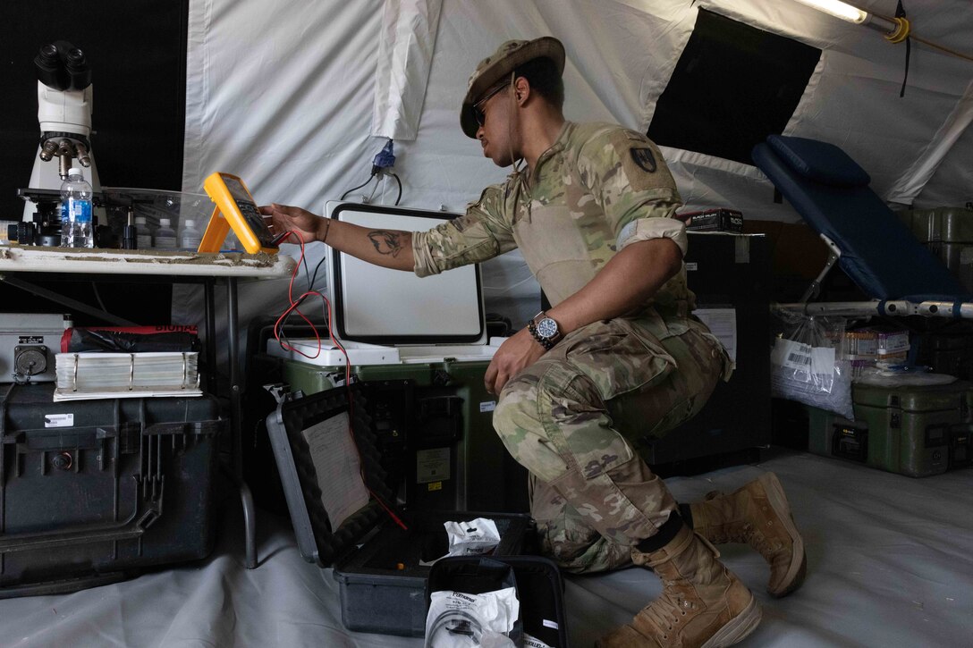 A soldier works on equipment while inside a tent.