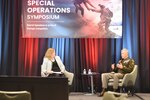 A soldier sitting in a chair speaks to a woman across from him.