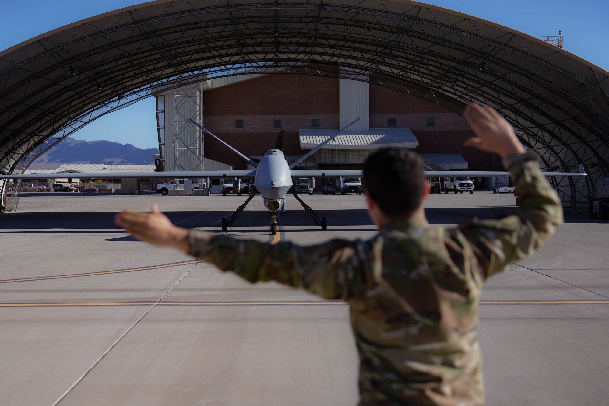 U.S. Air Force Airman 1st Class Raanan Reddinger, 432nd Aircraft Maintenance Squadron crew chief, marshals an MQ-9 Reaper before a training sortie, on Creech Air Force Base, Feb. 6, 2025. The 432nd AMXS ensures that Airmen, MQ-9 aircraft, ground control stations, and the global integrated communications network are fully mission capable to support aircrew training and combat operations. (U.S. Air Force photo by Staff Sgt. Jake Jacobsen)