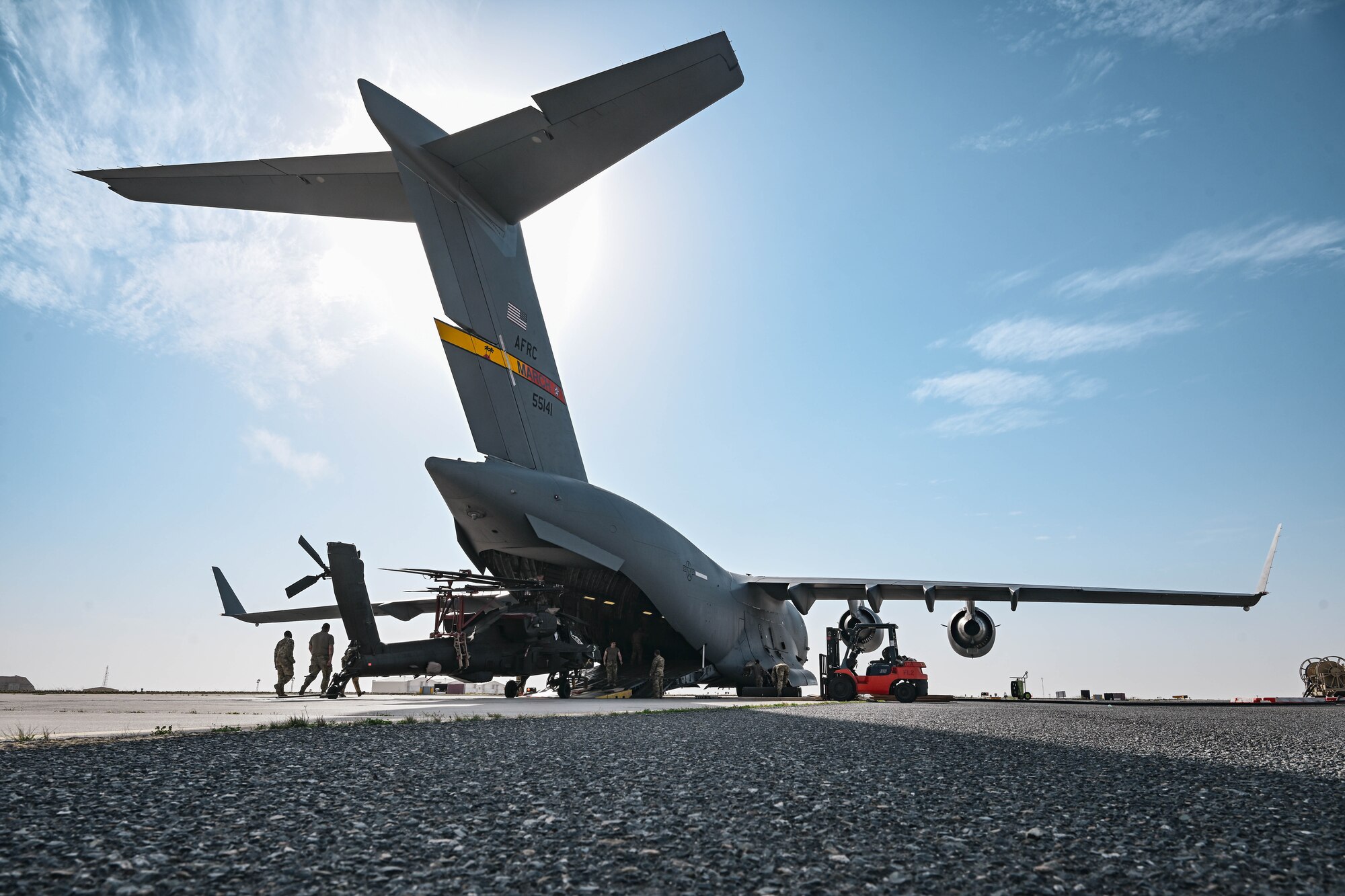 A military helicopter is loaded into a plane.