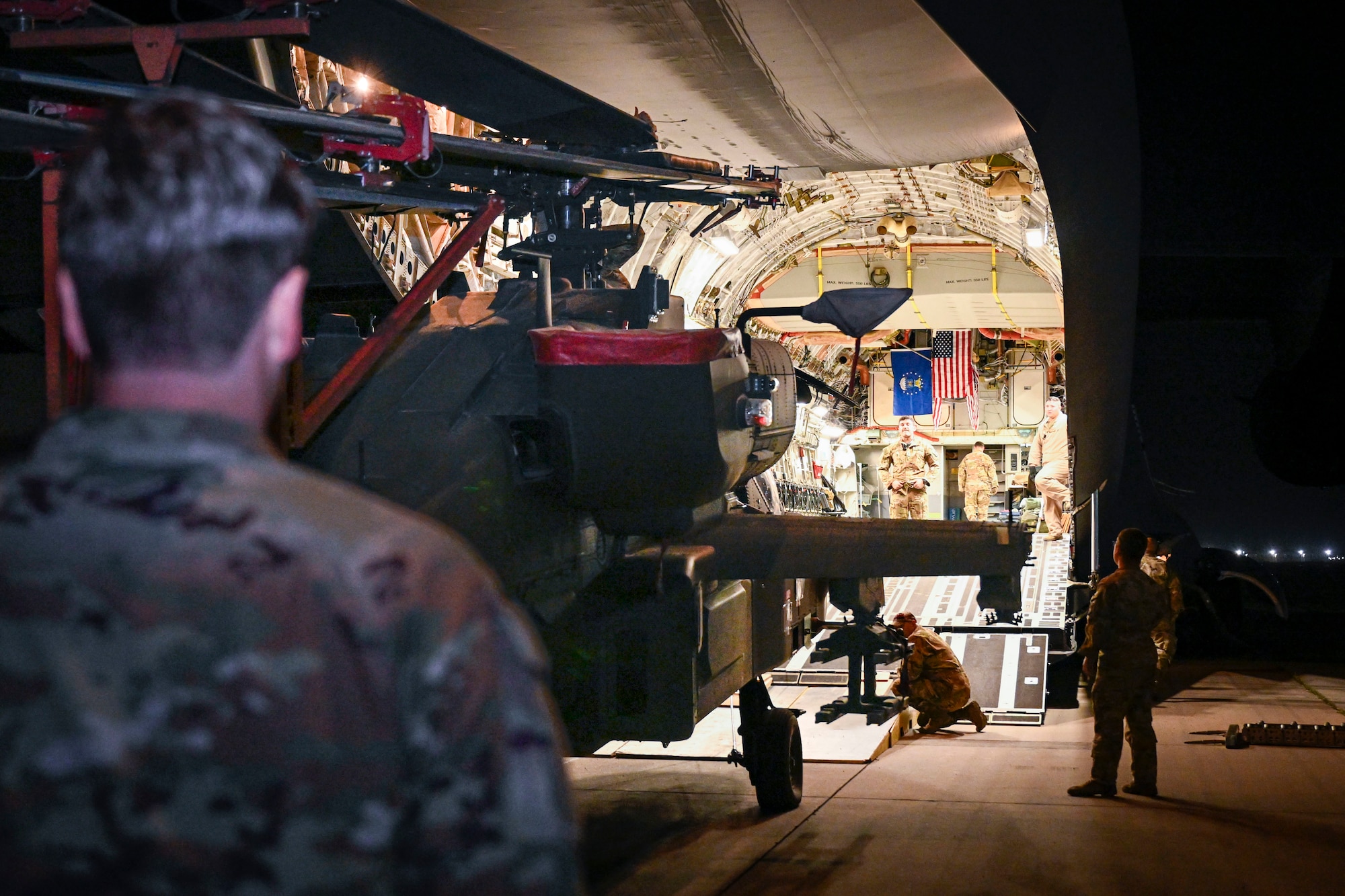 A man in uniform watches a helicopter being loaded into a plane.