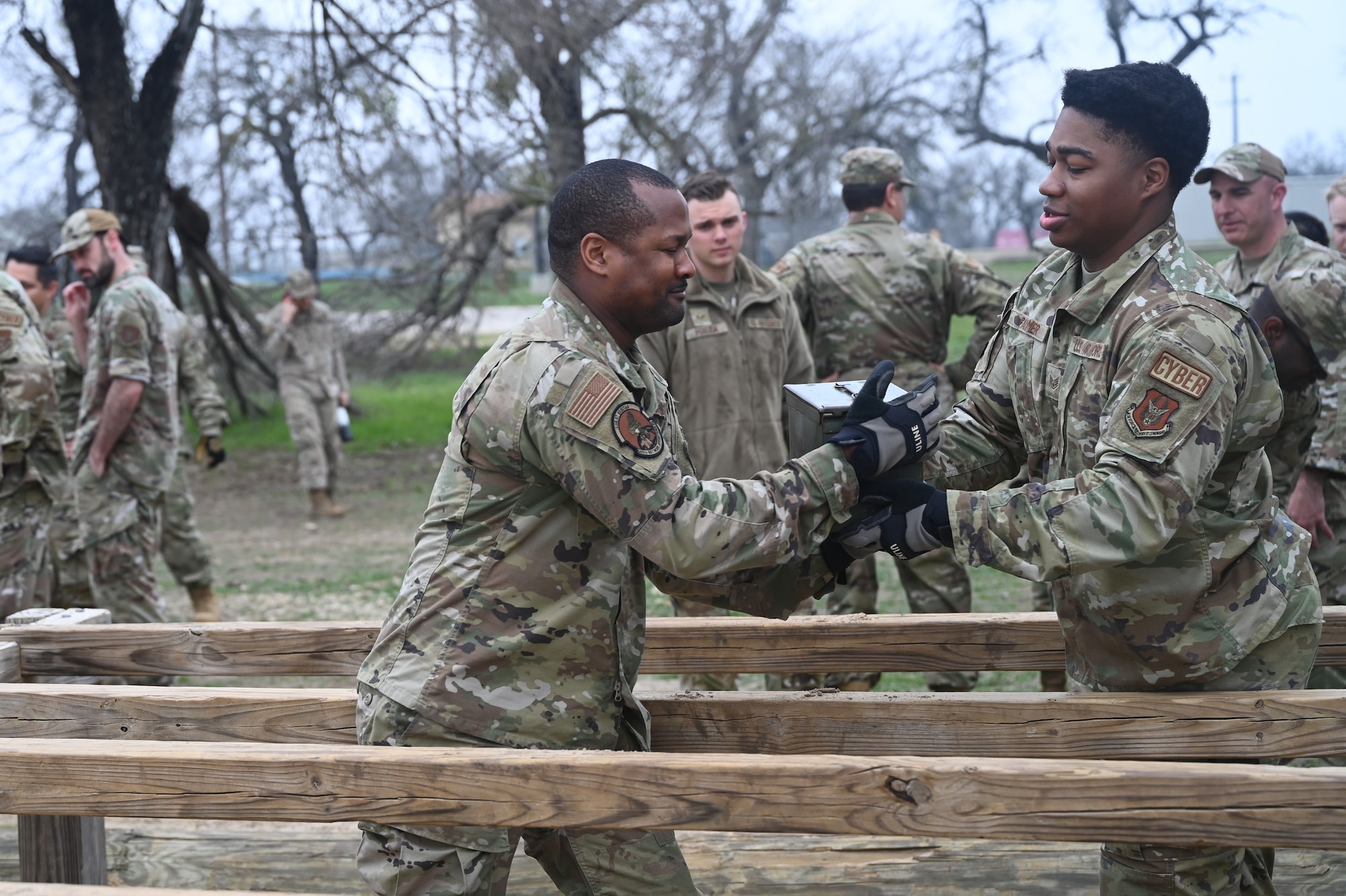 SSgt Kurtis Farmer passes a sand-filled ammunition container to Capt Cecil Calvin during a relay exercise at JBSA-Lackland, Texas on Feb. 9, 2024. The ‘six vaults’ obstacle is intended to be crossed using a series of high-steps without use of hands or significant delay in traversal. Participants are challenged during the final day by also alternating possession of the container which can weigh between 40 to 50 pounds. (US Air Force photo by Alex Dieguez)